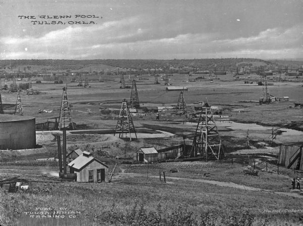 View from hill of oil derricks and steel tanks at Glenn Pool Oil Field where oil was first discovered on November 22, 1905 by Robert Galbreath and Frank Chesley. The Glenn Pool has produced 340 million barrels of oil since that day. Caption reads: "The Glenn Pool, Tulsa, Okla."