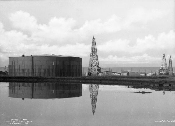 An oil derrick and a steel tank are reflected in a pool in Tulsa.