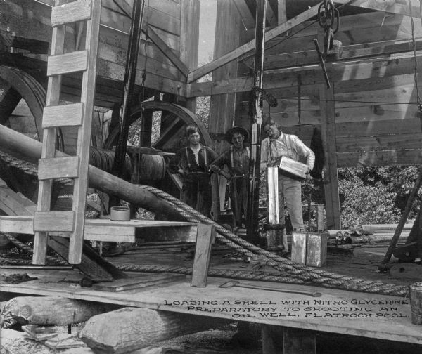 Three men load a shell with nitro-glycerine in preparation of shooting an oil well at Flatrock Pool, between the cities of Tulsa and Skiatook. Caption reads: "Loading a shell with nitro glycerine preparatory to shooting an oil well, Flatrock Pool."