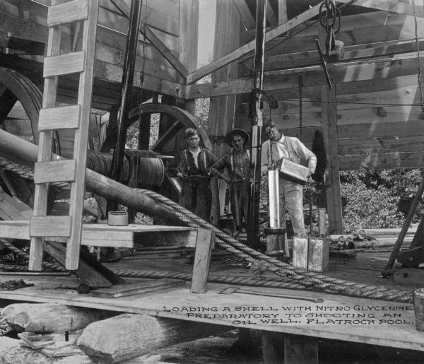 Three men load a shell with nitro-glycerine in preparation of shooting an oil well at Flatrock Pool, between the cities of Tulsa and Skiatook. Caption reads: "Loading a shell with nitro glycerine preparatory to shooting an oil well, Flatrock Pool."