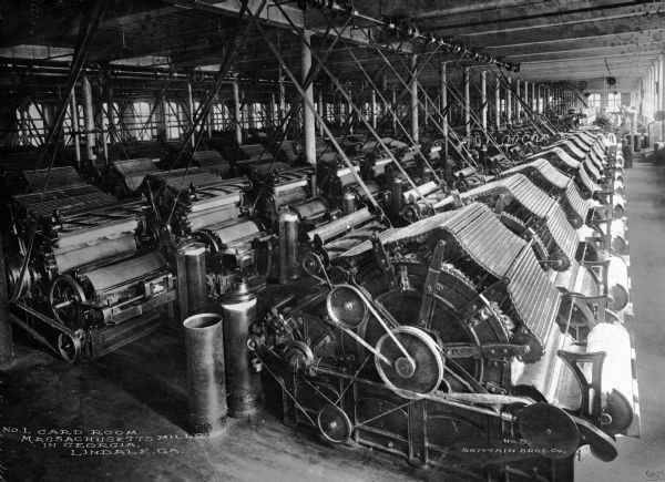 Slightly elevated view of large machines in the card room of Massachusetts Mill, which produced 1/7 of all textiles in Georgia.  Photograph published by Brittain Bros. Company. Caption reads: "No. 1 Card Room, Massachusetts Mills in Georgia, Lindale, GA."