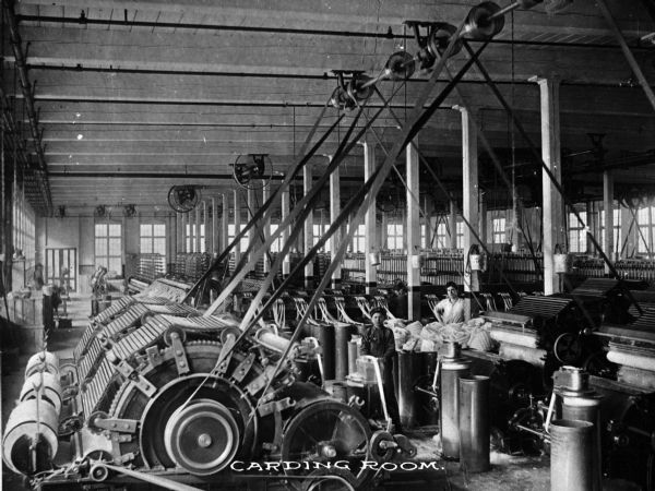 A young boy and a man are shown among the machinery in the carding room of the Pioneer Cotton Mill, which was in full operation by 1910, with W. H. Coyle as president. Caption reads: "Carding Room."