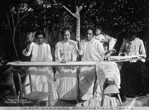 A group of women work at a loom outdoors. Caption reads: "Drawn Workers, Brownsville, Texas."