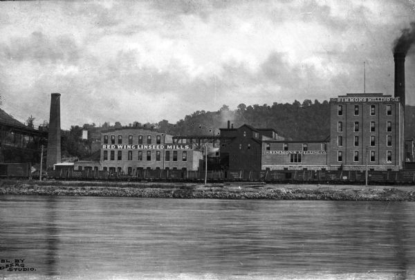 View across water toward buildings for the Red Wing Linseed Mills and the Simmons Milling Company.