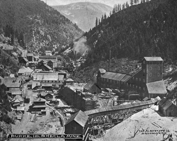 View of the Burke and Hecla Mine Buildings with mountains in the background. The company was incorporated in 1891. Caption reads: "Burke, ID. & Hecla Mine."