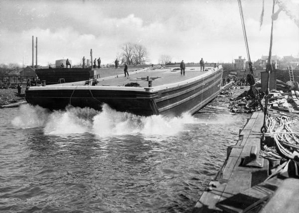 Men stand on a barge as it is being launched into a body of water.