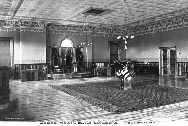 A view of antlers placed on the United States flag in the center of the lodge room of the Elks Club, founded in 1868. Caption reads: "Lodge Room, Elks' Building, Houlton, ME."