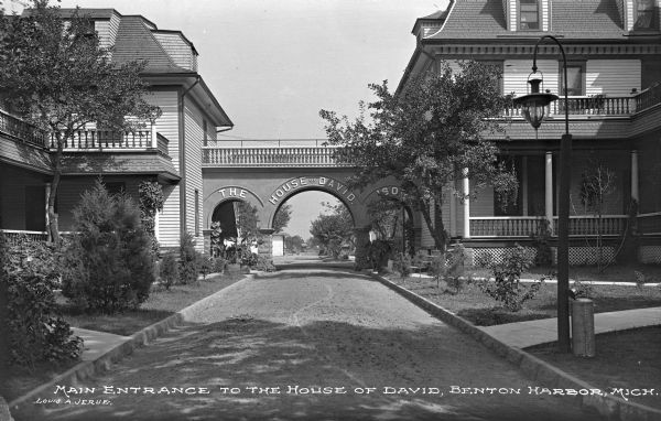 Front view of a bridge between two Victorian dwellings of The House of David, a religious commune founded in 1903. The bridge reads, "The House of David 1903." Caption reads: "Main Entrance to the House of David, Benton Harbor, Mich."