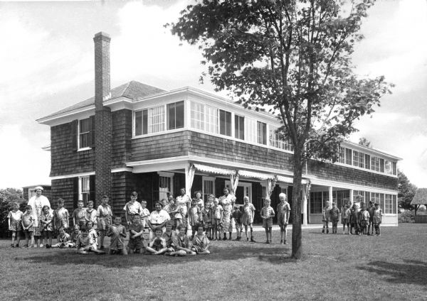 A view of children, adults, and a tree on the lawn in front of the Home for Crippled Children.