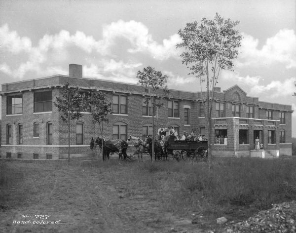 A view of children piled in a horse-drawn wagon in front of a children's home. The wagon reads, "Springfield Creamery Co." Women wait on the front steps of the home.