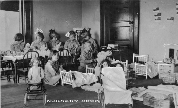 A view of young girls playing with dolls in the nursery of Pythian Orphans' Home. Caption reads: "Nursery Room."