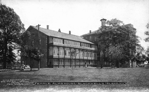 Exterior view of the Female Almshouse, a home for the aged and ill. A woman stands outside the door, and a telephone pole stands to the right of the building. Caption reads: "Female Alms House — Blackwell's Island, N.Y."