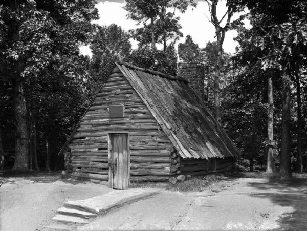 A view of a Continental Army hut in a wooded area. A set of steps lead to the front door.