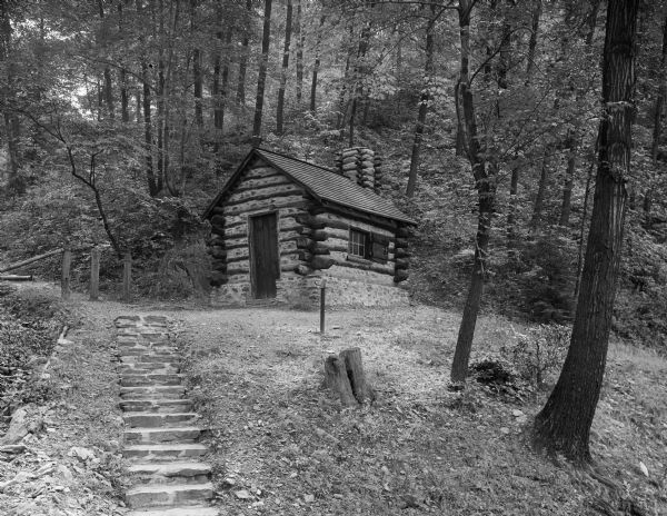 A set of stone stairs leads to a small soldiers' hut inhabited during the American Revolution. This view of the hut in a wooded area shows a door, a window, and a chimney.