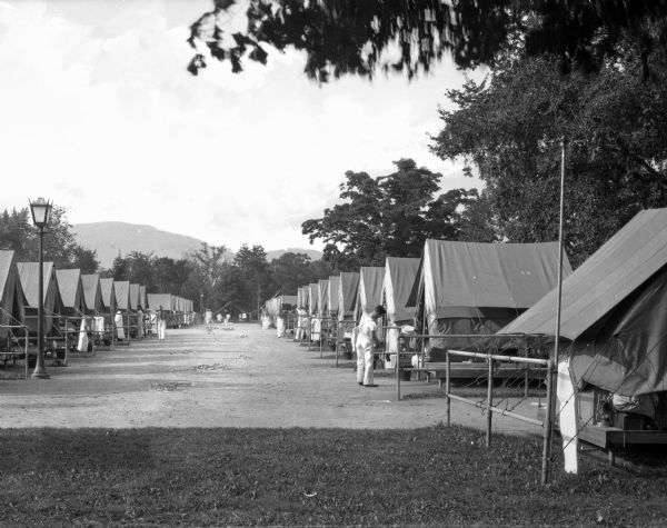 A view of two rows of tents at a U.S. Military Academy summer camp at West Point. A soldier stands by a tent in the row  on the right side.