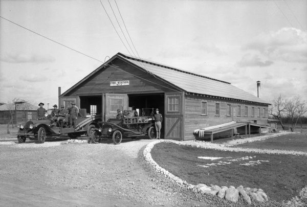 Men pose with two fire engines parked outside the open doors of the fire station at Camp Travis, named in 1917 after William B. Travis. The station sign reads: "Fire Station No. 3."