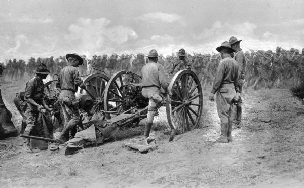 Soldiers stand by their artillery and the infantry marches to the right at Camp Travis, named in 1917.