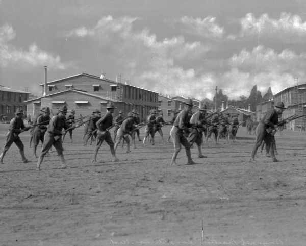A group of soldiers practicing with bayonets at Camp Meade, established in 1917.  The view includes military buildings behind the soldiers.