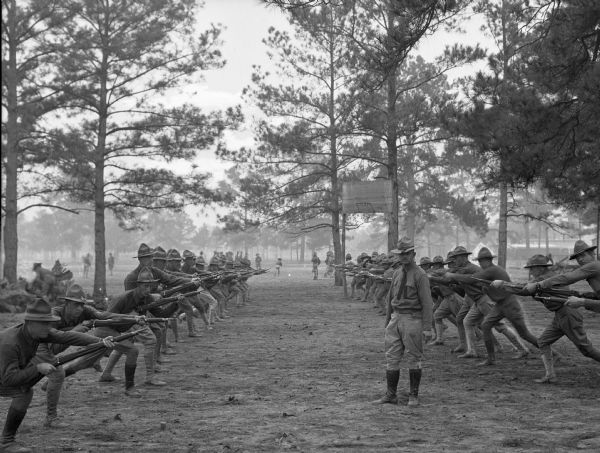 Two rows of soldiers face each other during a gun drill at Camp Logan.  A military officer stands in between the lines of men.