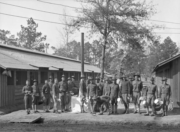 A view of soldiers standing between two military buildings of Camp Logan, holding dishes and waiting for dinner.