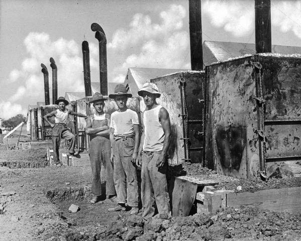 A view of four men standing near a row of Army baking ovens at Camp Bowie, built in 1917.