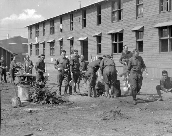 A view of soldiers standing outside a military building at Camp Upton, built in 1917, doing dishes.