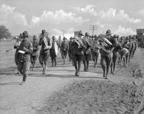 The 316th Regimental Band marching down a dirt path at Camp Meade, established in 1917.  Telephone poles are visible in the background.