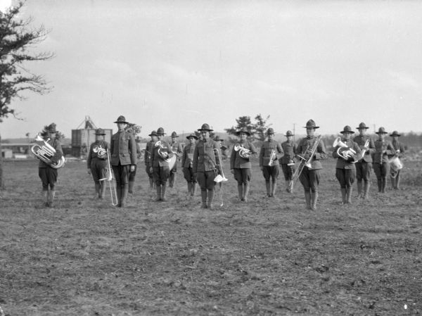A formation of uniformed men holding musical instruments in a field at Camp Devens, established in 1917.