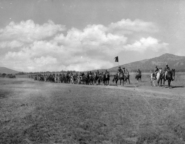A group of soldiers on horseback executing field artillery maneuvers at Camp Doniphan, activated for artillery training during World War I.  The man leading the drill holds a flag.