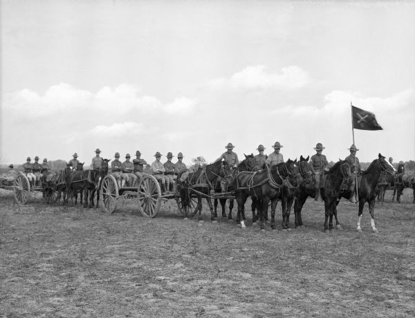 A view of hores-drawn artillery and wagons. The man leading the artillery drill carries a flag.