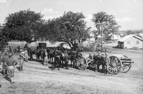 A view of horse-drawn light artillery at Camp Travis, named in 1917.  The view includes parked automobiles and camp dwellings.