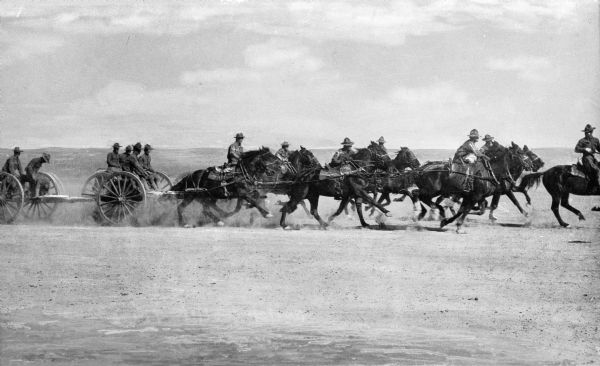 Soldiers transporting artillery across a plain on horseback at Camp Travis, named in 1917.