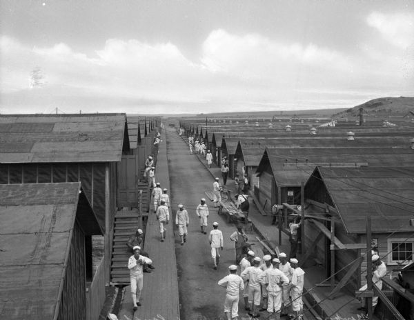 A view of sailors in uniform standing between the rows of barracks of the United States Naval Training Station.