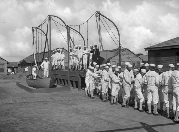 A view of sailors during land training on boat hauling at the United States Navy Camp Wissahickon.  Military buildings stand behind the men.