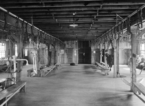 A view of the seamanship instruction hall at the United States Navy Camp Wissahickon. Equipment lies on either side of the room, and men sit against the right wall.