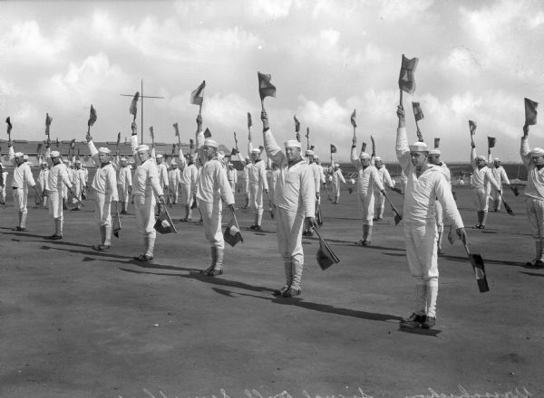 A view of rows of sailors holding two flags during a semaphore drill at the United States Navy Camp Wissahickon.