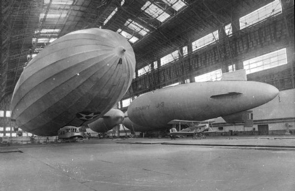 A view of the interior of airship Hangar No. One at the Naval Air Station.  The "Los Angeles," completed in 1924, is found on the left, and a J-3 blimp, first flown in 1926, can be seen on the right.  Between the "Los Angeles" and the J-3 blimp, a smaller aircraft stands on the ground of the hangar.
