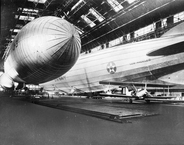 A view of the interior of airship Hangar No. One at the Naval Air Station. The "Los Angeles," completed in 1924, is found on the right, and a J-3 blimp, first flown in 1926, can be seen on the left. Between the "Los Angeles" and the J-3 blimp, a smaller aircraft stands on the ground of the hangar.