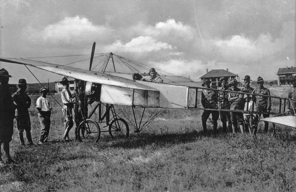 A view of men posing around a bomber, manufactured by Handley Page Limited, a company founded in 1909.  Behind the bomber stand the military buildings of Camp Vail, named in September, 1917.
