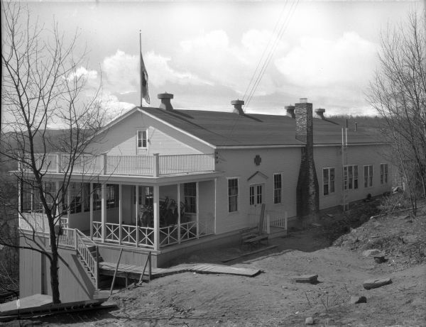 Exterior view looking down toward the Nurses' Recreation House at the United States Army General Hospital. A flag on a flagpole is on the roof, and a man is standing on the porch.