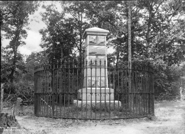 View of a monument to Stonewall Jackson (1824-1863), American Civil War Confederate General. The memorial, erected in 1888, stands in a wooded area, surrounded by a fence.