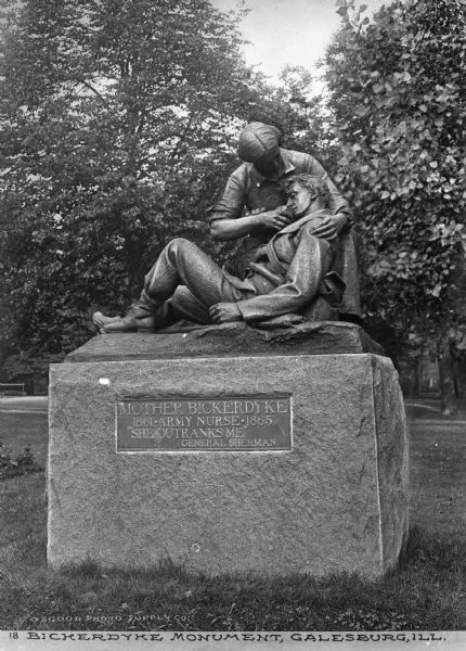 View of a monument to Mother Bickerdyke (1817-1901), an army nurse. The memorial, erected in 1904, features Mary Ann Bickerdyke kneeling beside a soldier, holding a cup to his lips. The quotation by General Sherman on the base of the monument reads, "She outranks me." Caption reads: "Bickerdyke Monument, Galesburg, Ill."