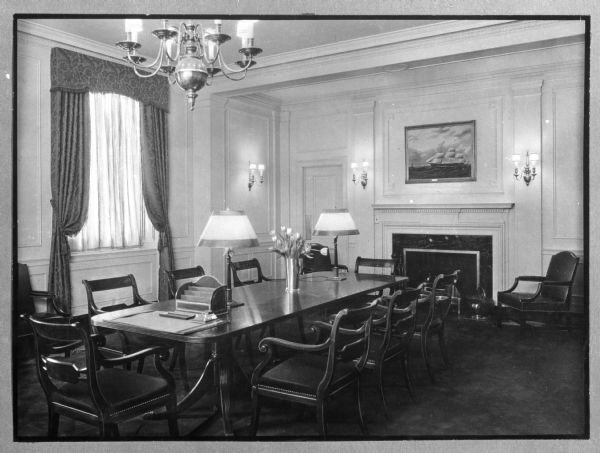 Interior of the Director's Room at the Doctor's Hospital, founded by Theodore Atlas in the early 1900's. The view includes a long table with chairs surrounding it, and a window and a fireplace behind it.