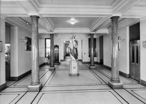 Interior of the lobby at Saint Mary's Hospital, completed May 18, 1859 and designed by Anthony Bley. The view includes a statue of Mary and Jesus surrounded by four pillars.  Signs read, "Pharmacy" on the left, and "Telephone" on the right.
