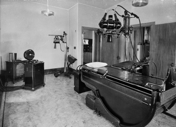 Interior of the x-ray department at Saint Mary's Hospital, completed May 18, 1859 and designed by Anthony Bley. An x-ray machine and table can be seen, as well as other medical equipment. Two doors are in the back right corner.