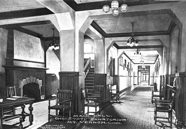 Interior of the main hall at the Ohio State Sanatorium, which opened in 1909. The view of the main hall includes a long entryway, a seating area, and stairs leading upward on the left, near a fireplace. Caption reads: "Main Hall, Ohio State Sanatorium, Mt. Vernon, Ohio."