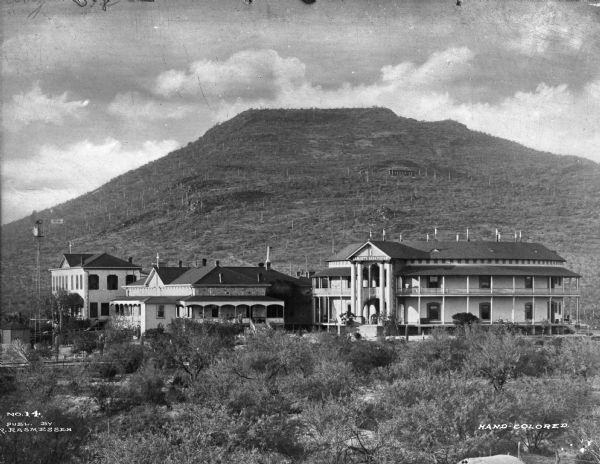 Exterior of Saint Mary's Sanatorium, founded in 1880 by Bishop Salpointe. The view shows a two-story rotunda on the right, and two other buildings of the sanatorium to the left. A hill rises in the background.