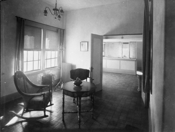 Interior of a sitting place at Saint Mary's Sanatorium, founded in 1880 by Bishop Salpointe. The view includes a table and two chairs, and opened double doors are open to another room.