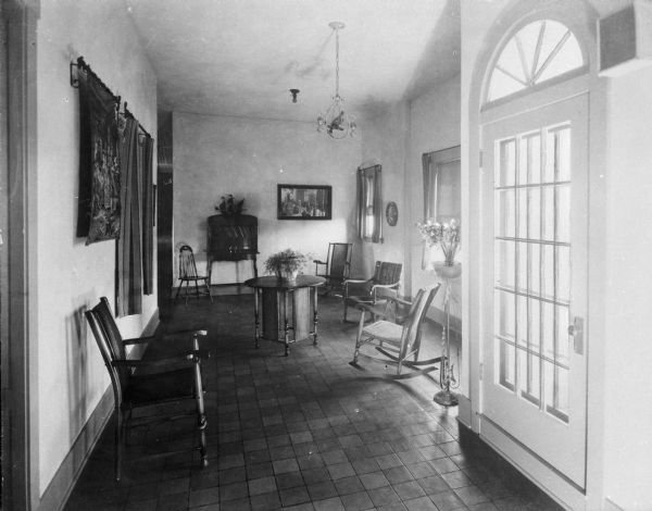 Interior view of a sitting room at Saint Mary's Sanatorium, founded in 1880 by Bishop Salpointe. The room holds chairs and a table, and a door with a fan window is in the foreground on the right.