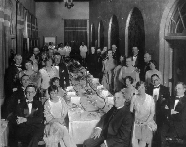 Slightly elevated view of a group of patients in formal dress gathering around a long table for dinner at Saint Mary's Sanatorium, founded in 1880 by Bishop Salpointe.